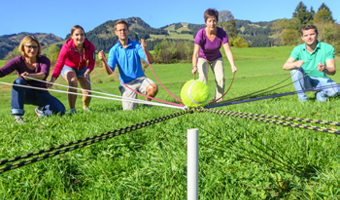 Eine Gruppe von fünf Personen konzentriert sich, einen Tennisball gemeinsam mittels Schnüren und Bändern abzulegen. Es gilt gemeinsam etwas zu schaffen.