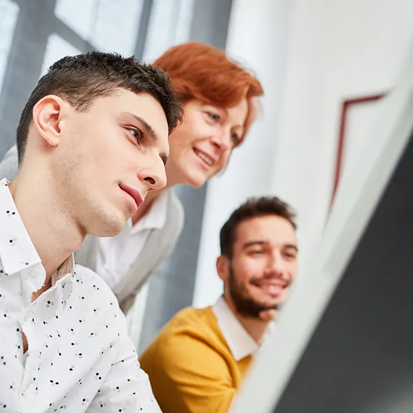 Ausbilderin erklärt zwei Jugendlichen etwas am PC 